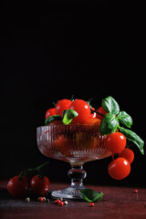 Juicy cherry tomatoes with basil in a vintage bowl on dark rustic table, ideal for clean eating and plant-based lifestyle