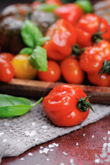 Ripe tomato with sea salt and basil on a textured kitchen towel and red countertop, promoting healthy organic eating