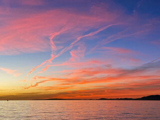 Sea sunset after the sun has set behind the horizon. Numerous cirrus clouds of different shapes and colors in the sky. Calm sea. Rocky shores on the horizon. Arenal. Mallorca Island. Spain.