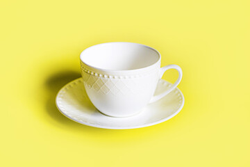 white beautiful tea cup with a pattern on a white saucer stands neatly on a yellow background in the center