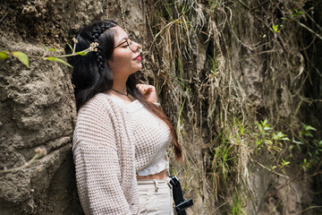 A young woman savors a tranquil moment beside a mosscovered rock, enveloped by an array of vibrant...