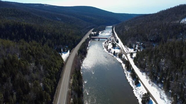 Panoramic view of the Routhierville Covered Bridge spanning the legendary salmon fishing river, the Matapedia River, through a snow-covered mountain valley. Quebec, Canada, Winter 2025.