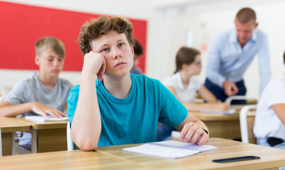 Portrait of focused teenage student writing lectures in workbooks in classroom during lesson..