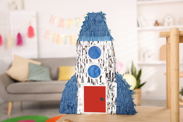 Bright pinata in shape of rocket on wooden table in festive decorated room
