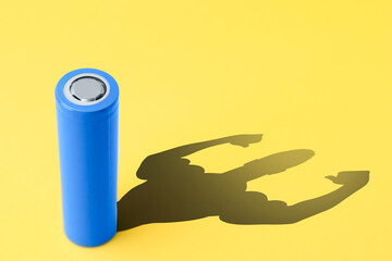 Alkaline battery with shadow in shape of strong muscular man on yellow background