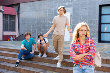 Sad young girl with backpack standing near school building. She's offended by her friends who...