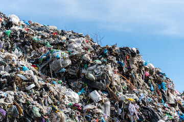 A large mound of mixed waste materials rises against a backdrop of blue sky, illustrating the...