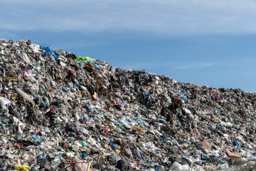 Massive pile of trash dominates the landscape, showcasing plastic materials and other waste in a landfill site against a bright sky