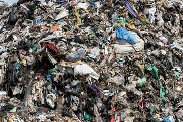 A massive pile of garbage fills a landfill site, consisting of various types of waste, located near a bustling city. The sight emphasizes waste management issues