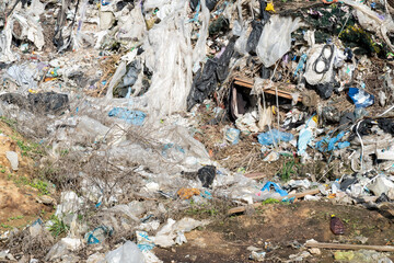 A disturbed landscape shows heaps of plastic and waste cluttering the ground, endangering local flora and fauna in a secluded area during daylight hours