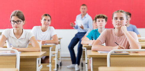 Smart teenagers studying in classroom, listening to lecturer and writing in notebooks..