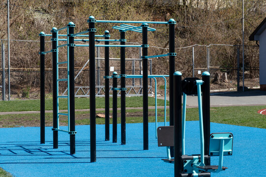 Various fitness stations are set up in a community park, featuring colorful equipment on a blue surface, inviting people to exercise outdoors in springtime