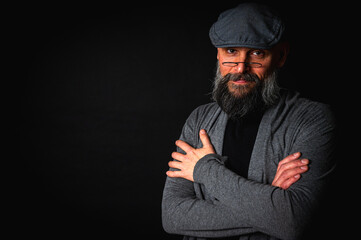 Close-up portrait of a serious bearded man in flat cap and glasses on black background. Stylish, intense look with confident and mysterious expression