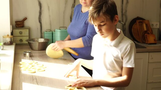 Boy with mother prepare dough for donuts at the kitchen