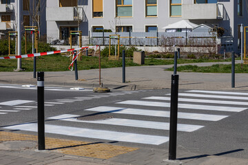 Newly renovated pedestrian crosswalk in modern residential area with safety bollards, fresh white...