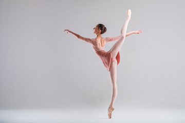 young slender ballerina in pointe shoes and a pink leotard dances on a white background