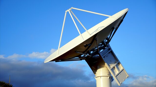Large parabolic radar antenna pointing at the blue sky with few clouds, used for aerospace applications, satellite communications, and telecommunications
