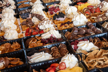 Variety of fresh baked waffles richly decorated with different toppings, sweet sweets, chocolate, cream, fruit and berries, jelly sweets in bakery with confectionery shop, old Volendam, Dutch sweets