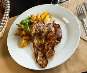 Grilled beef steak with potatoes and green peppers view from above. Serving a cooked piece of meat with vegetables on a white plate for lunch