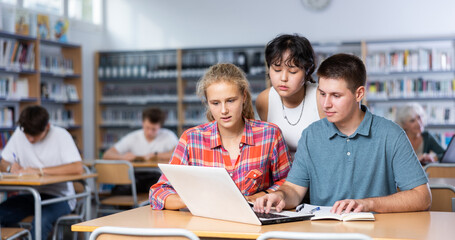 Interested teenagers studying in information technology class at college library, sitting around...
