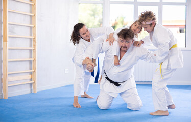 Children with parents practicing judo together on sports mats in gym
