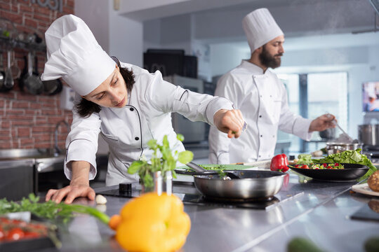 In a kitchen, woman chef perfecting a gourmet meal by adding fresh herbs, balancing flavors with basil and other condiments. Kitchen counter stocked with vegetables and food prep essentials.