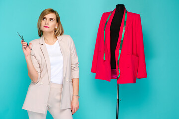 fashion designer with scissors standing beside bright red blazer on mannequin in creative studio....