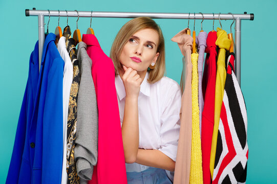 thoughtful woman between colorful clothes, considering fashion choices on clothing rack. bright garments on hangers create vibrant wardrobe scene for style inspiration and decision-making