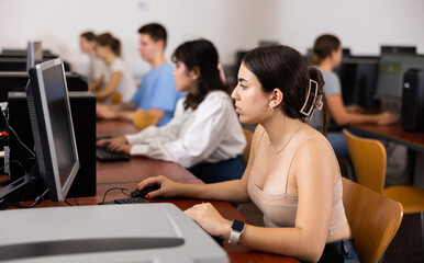 Fototapeta premium Teenage girl sitting at table and using computer during lesson.