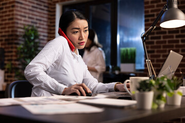 Focused businesswoman multitasking in modern office environment. Dedicated female executive talking...