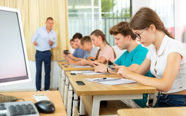 Interested teen girl student using smartphone while studying in college with group of classmates..