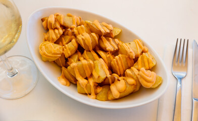 Spanish dish, patatas bravas, fried potatoes served with spicy sauce on plate.