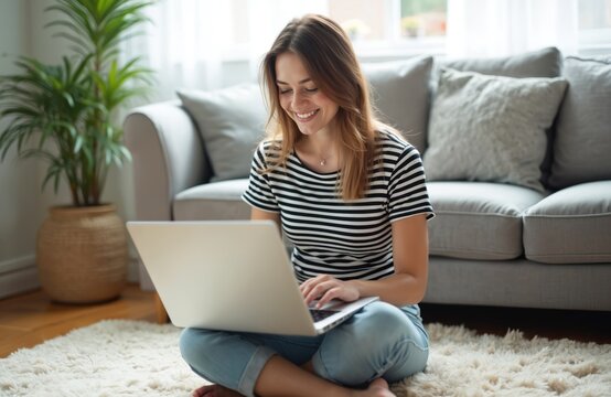 Young attractive woman uses laptop sitting floor at home. Female browsing internet, smiling, typing in casual attire. Digital nomad working remotely, surfing web, enjoys cozy home. Modern tech