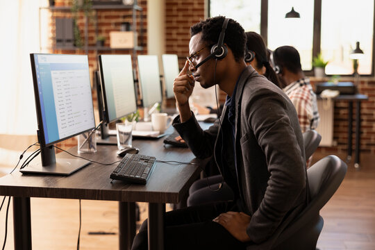 Male customer support agent looking at computer screen showing financial data and statistics, tracking performance ratings. African american man, focused in his work, reviewing data on desktop monitor