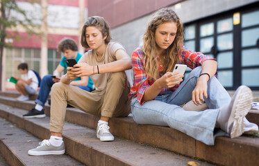 Schoolers boy and girl using gadgets on break outside college on sunny day
