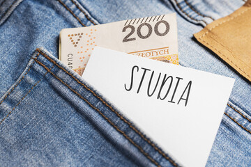 White card with a handwritten inscription "Studia", put into the pocket of blue pants jeasnow, next to Polish banknotes PLN (selective focus), translation: Studies