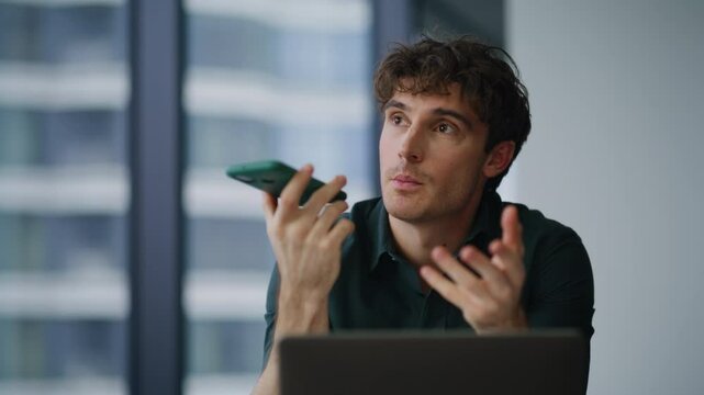 Freelancer dictating voice message at smartphone sitting agency office closeup.