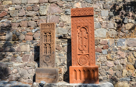 Ornate stone crosses khachkars intricately carved with decorative patterns stand in front of aged, rocky background, showcasing historical artisan craftsmanship and cultural heritage. Geghard Armenia