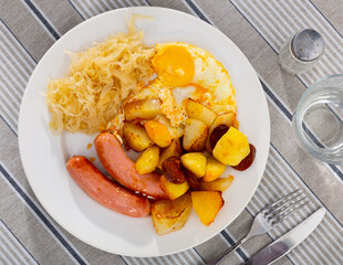 Sausages with fried eggs, potatoes and pickled cabbage served for breakfast