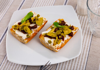 Healthy sandwiches for breakfast or lunch with toasted baguette, cream cheese spread, slices of sun-dried tomatoes, green olives and pesto. Mediterranean style vegetarian appetizers