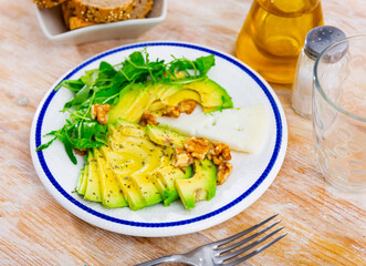 Avocado fruit is peeled and cut into slices on plate. Vegetarian snack complemented with cheese and walnut. View from above. Healthy, easily digestible snack, fruit food, energy source