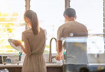 Couple washing the dishes together doing home chores housework, family togetherness concept