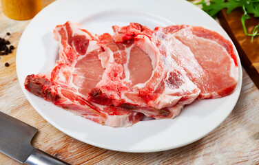 Slices of uncooked pork loin on white circular plate.