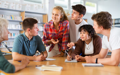Group of schoolchildren discussing together in library and preparing for school exam