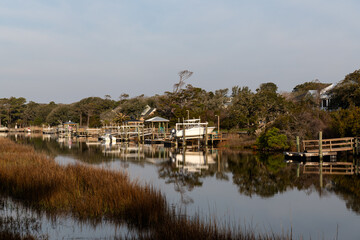 OAK ISLAND, NC, USA - March 13, 2025: Docked boats reflect in the still waters of a peaceful canal lined with homes and trees.