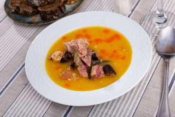 delicious pea soup with smoked meats and orange carrots cools down in white ceramic plate