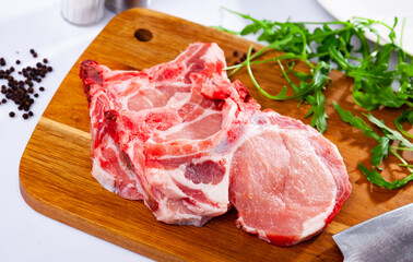 Raw meat, fresh pork loin chops with arugula and black pepper on white table