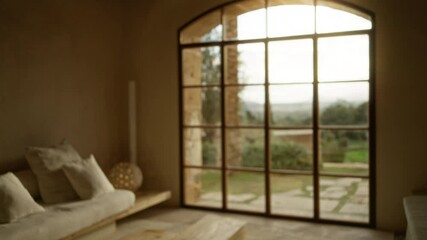 Luxury mediterranean home with blurred furniture and large window offering scenic outdoor view in a serene indoor setting focusing on a comfortable lounge area.
