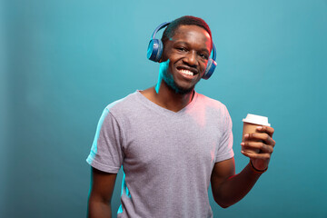 African american male individual stands with a disposable cup, listening to music on his wireless...