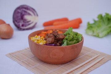 a colorful and appetizing bowl of food, placed on a bamboo mat with a pair of chopsticks beside it